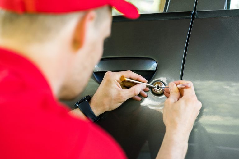 Locksmith In Red Uniform Opening Car Door With Lockpicker